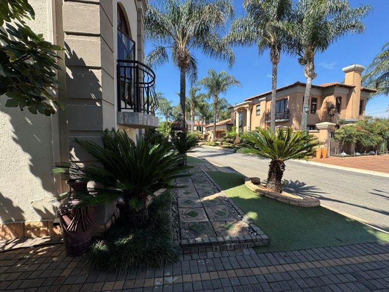 A street-level view of a residential estate featuring paved driveways, manicured landscaping, and Mediterranean-style architecture with wrought iron balcony details.