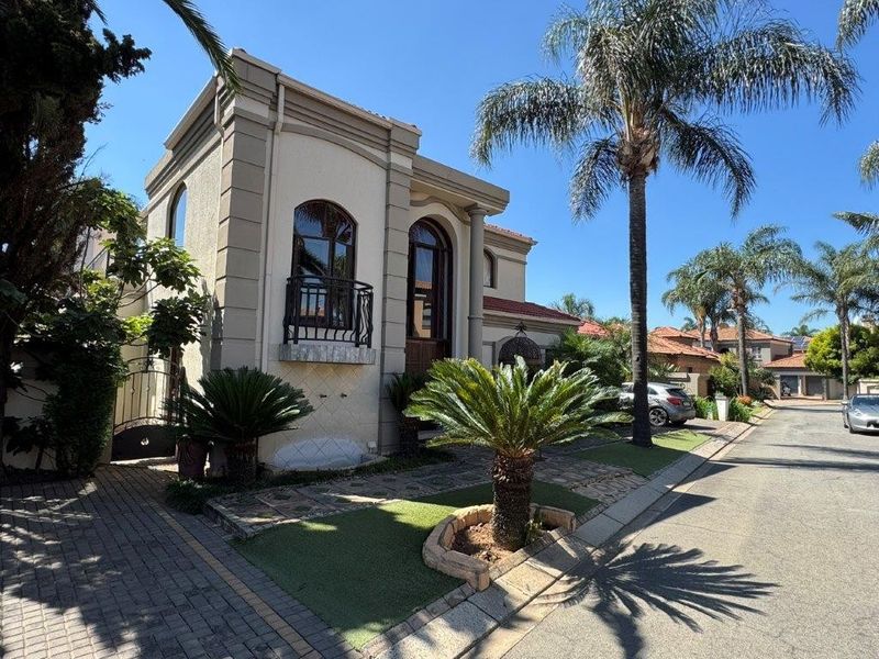 A well-maintained two-story residential facade featuring arched windows, a decorative wrought iron balcony, and a paved driveway with landscaped garden elements.