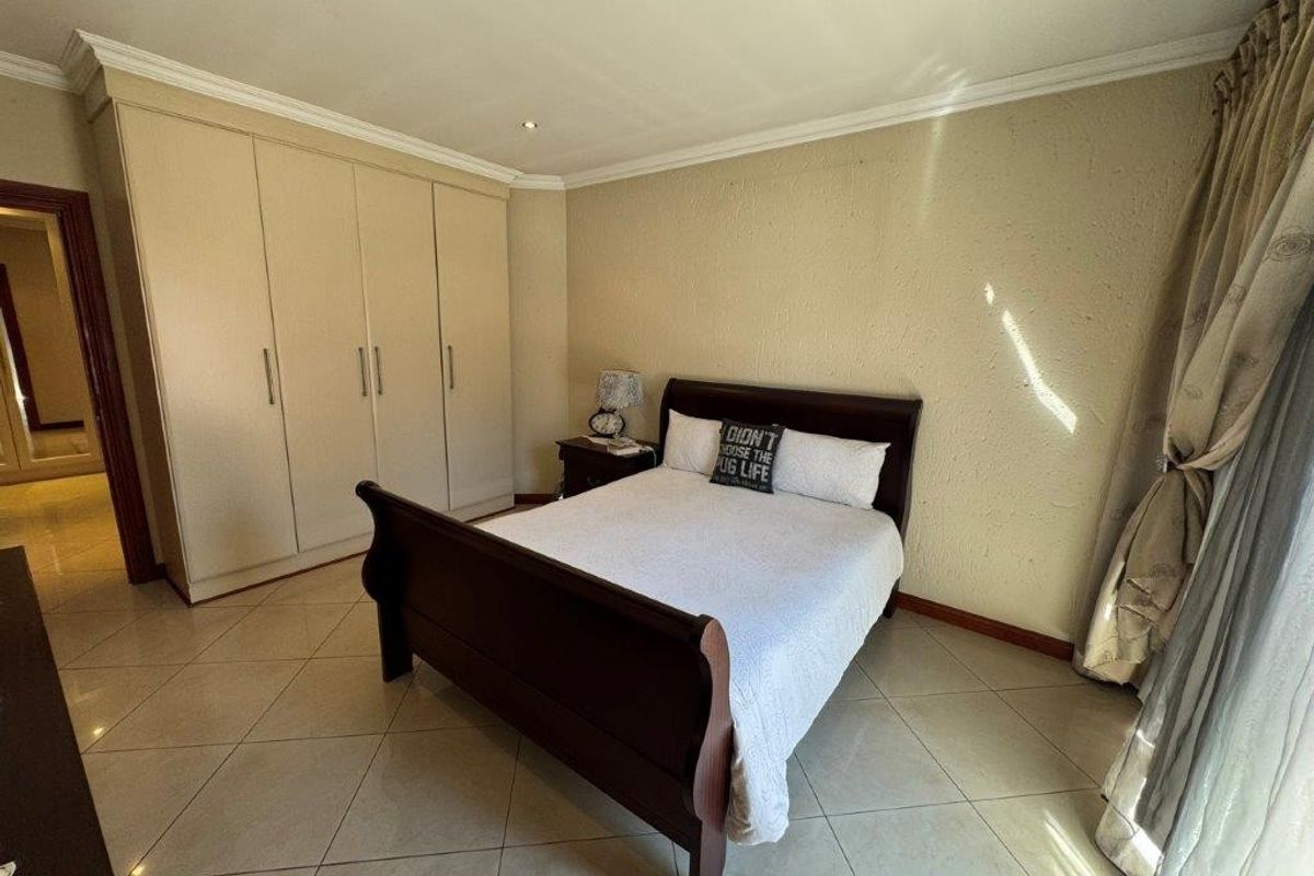 A well-maintained bedroom featuring neutral tiled flooring, built-in cupboards, and recessed downlighting, offering a clean and functional living space.