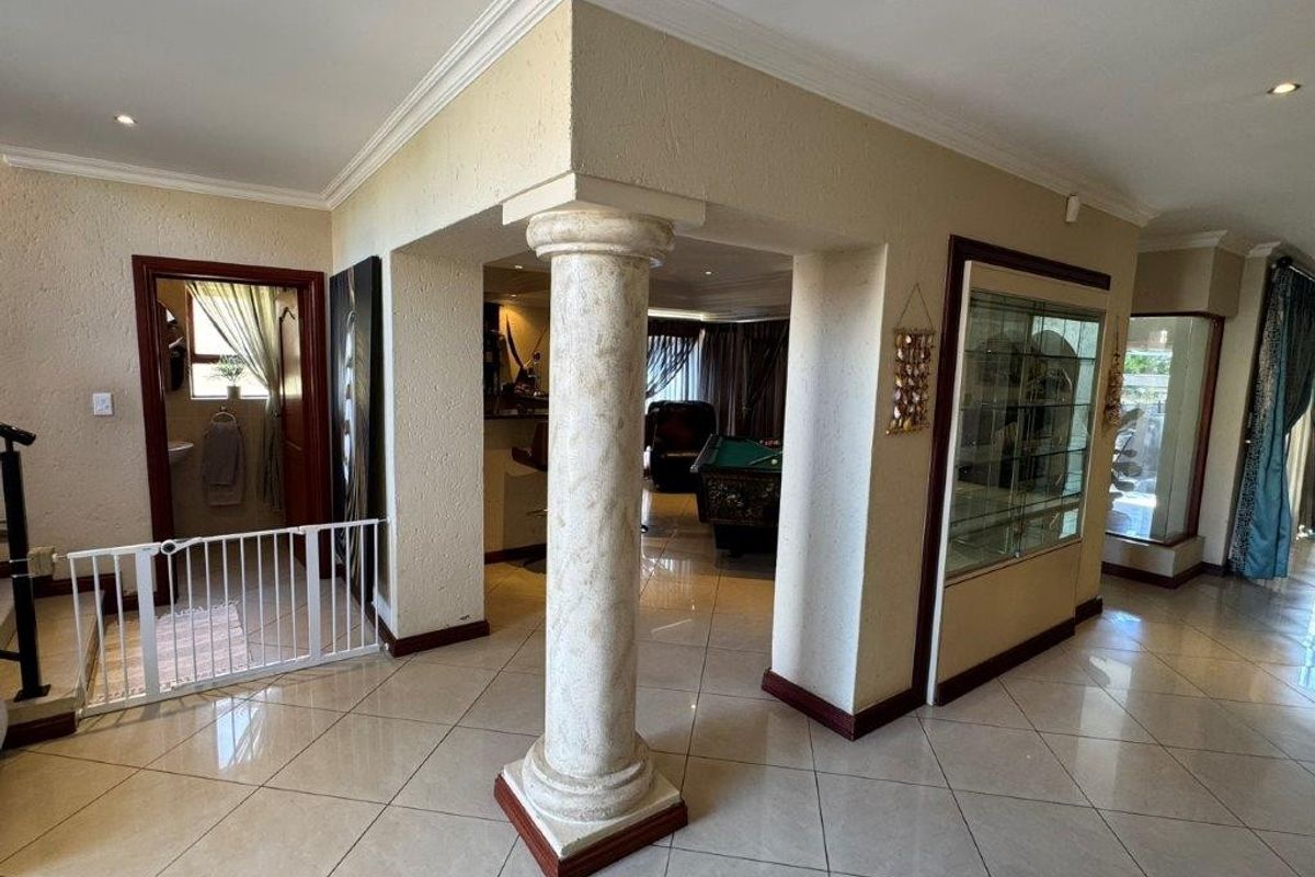 Spacious living area featuring tiled flooring, decorative columns, and built-in display cabinetry with recessed lighting and crown molding details.