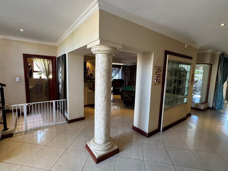 Spacious living area featuring tiled flooring, decorative columns, and built-in display cabinetry with recessed lighting and crown molding details.