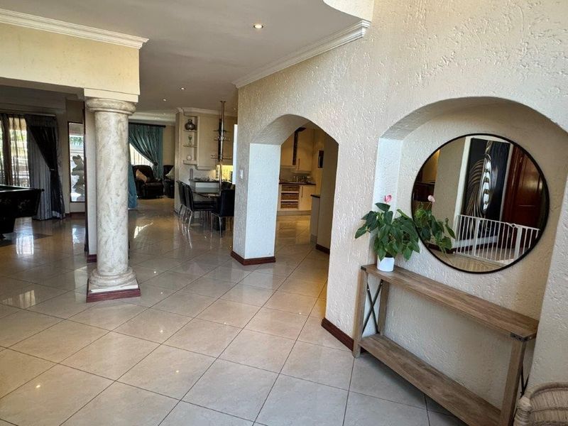 Spacious open-plan living area featuring tiled flooring, decorative columns, and arched architectural details connecting the main living space to the kitchen and dining area.