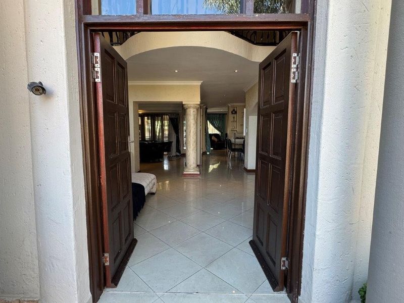 Inviting entrance featuring double wooden doors opening into a spacious, tiled interior with an elegant archway and decorative column.