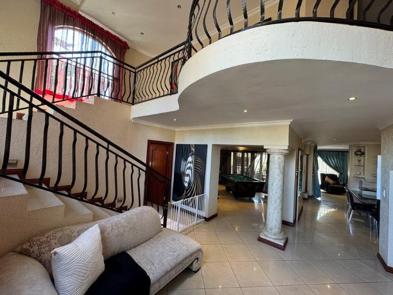 Spacious grand entrance hall featuring a sweeping staircase with wrought iron railings, tiled flooring, and an open-plan layout leading to adjacent living areas.