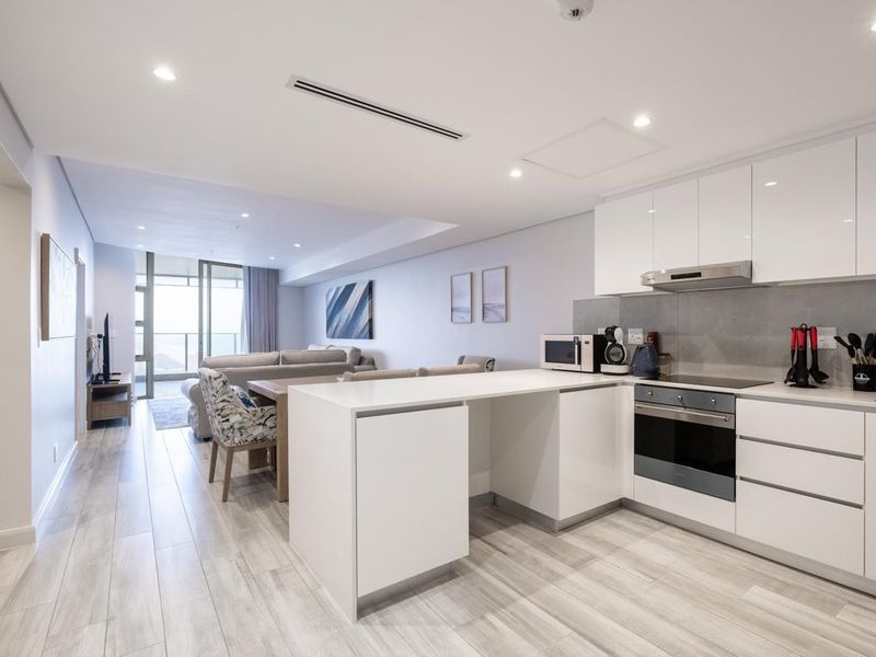 Modern open-plan living area featuring a sleek kitchen with white gloss cabinetry, integrated appliances, and ducted air conditioning, flowing into a bright living space.