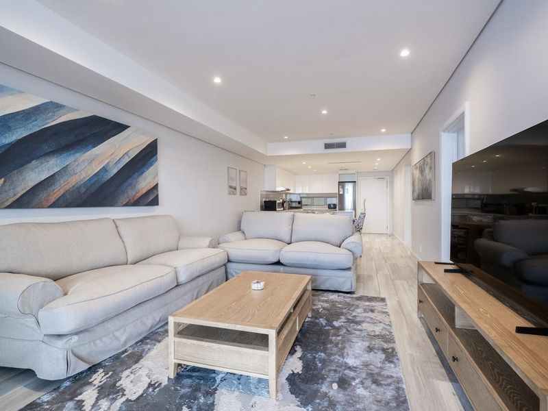Modern open-plan living area featuring neutral tones, recessed downlighting, ducted air conditioning, and seamless flow into a contemporary kitchen space.