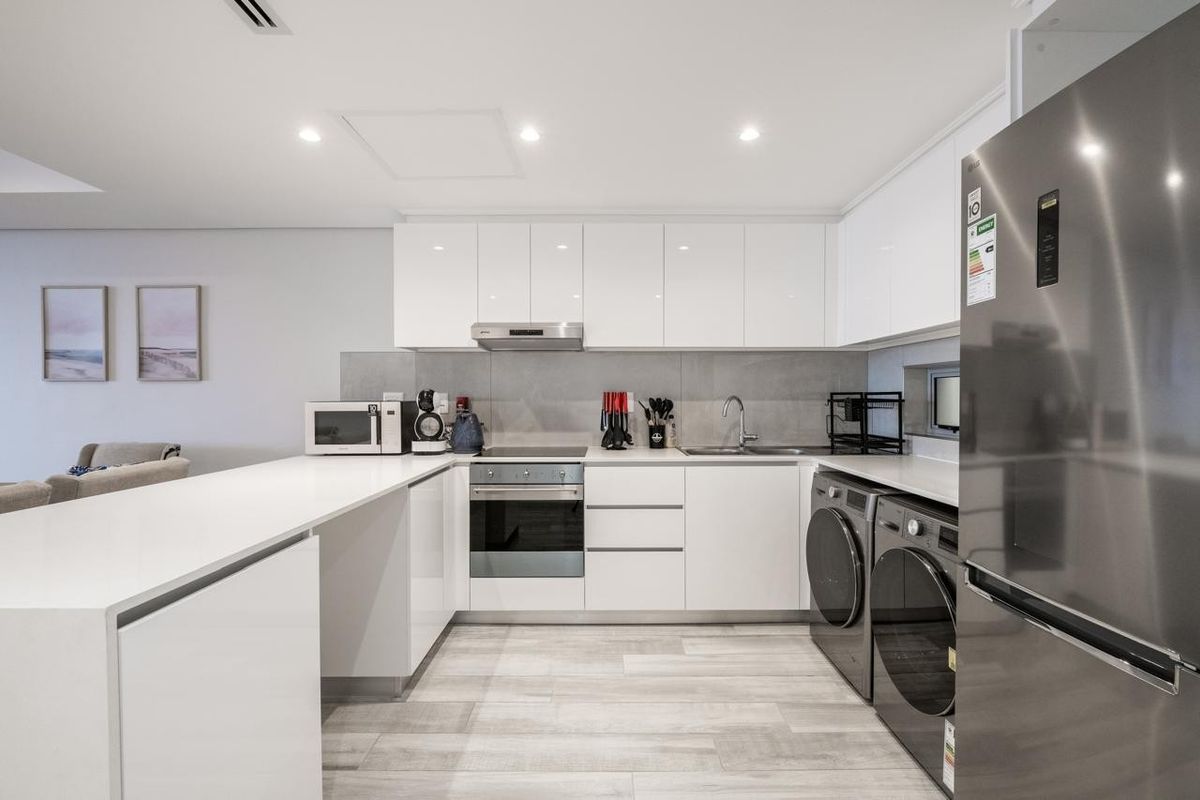 Modern kitchen featuring sleek white cabinetry, stone countertops, integrated appliances, and a clean tiled backsplash in a bright, open-plan layout.