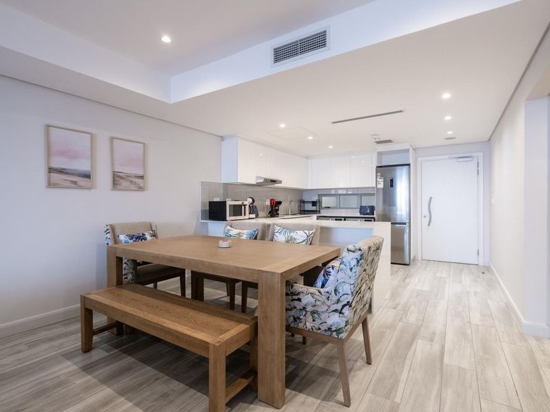 Modern open-plan apartment featuring a sleek kitchen with stone countertops, integrated cabinetry, and ducted air conditioning, seamlessly flowing into the dining area.