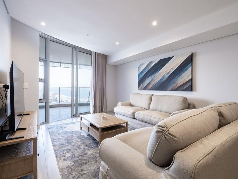 Modern living room featuring laminate flooring, recessed downlighting, and large sliding glass doors providing access to a private balcony with coastal views.