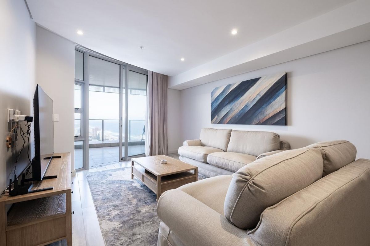 Modern living room featuring laminate flooring, recessed downlighting, and large sliding glass doors providing access to a private balcony with coastal views.