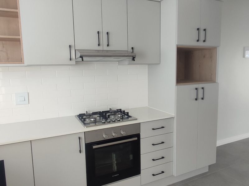 Modern kitchen featuring light grey cabinetry, stone countertops, subway tile backsplash, and integrated stainless steel appliances including a gas hob and oven.