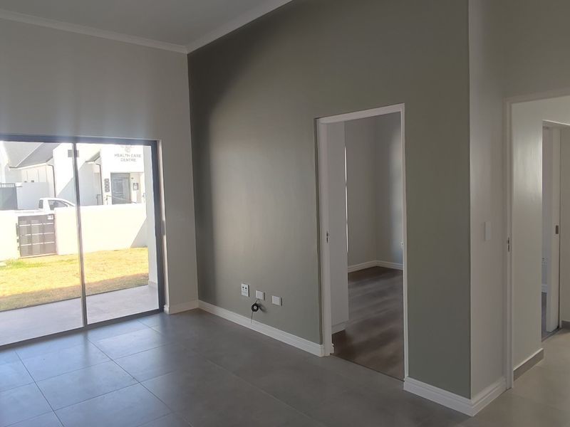 A bright, modern, and empty living area featuring large sliding glass doors, neutral grey tiled flooring, and clean, contemporary wall finishes.