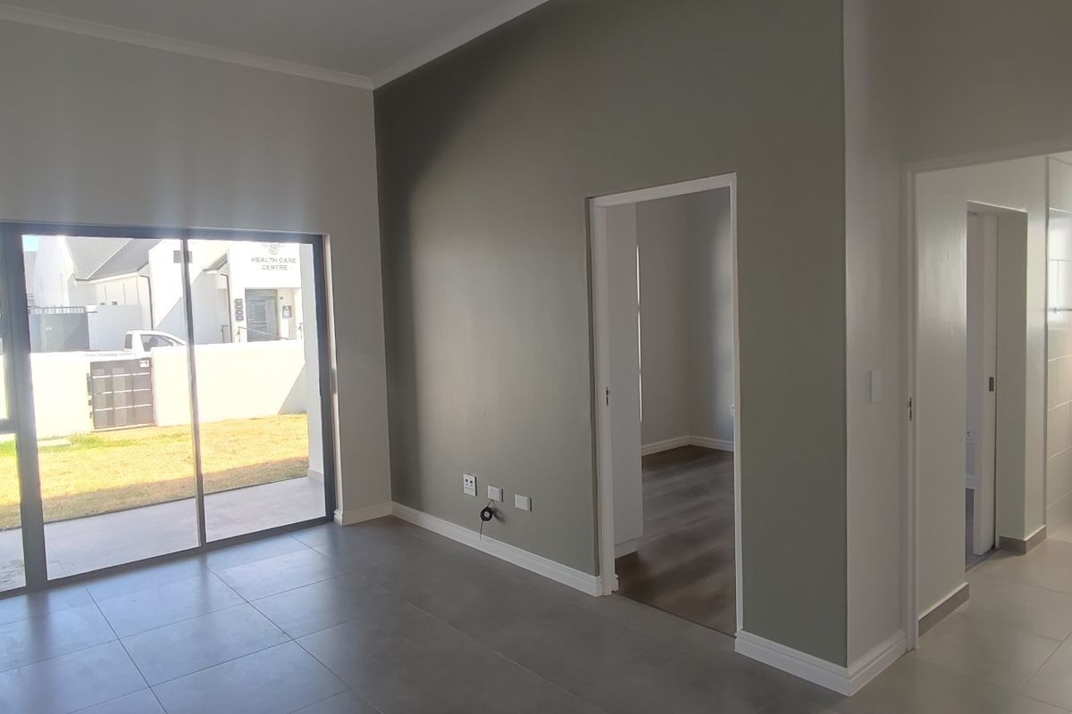 A bright, modern, and empty living area featuring large sliding glass doors, neutral grey tiled flooring, and clean, contemporary wall finishes.