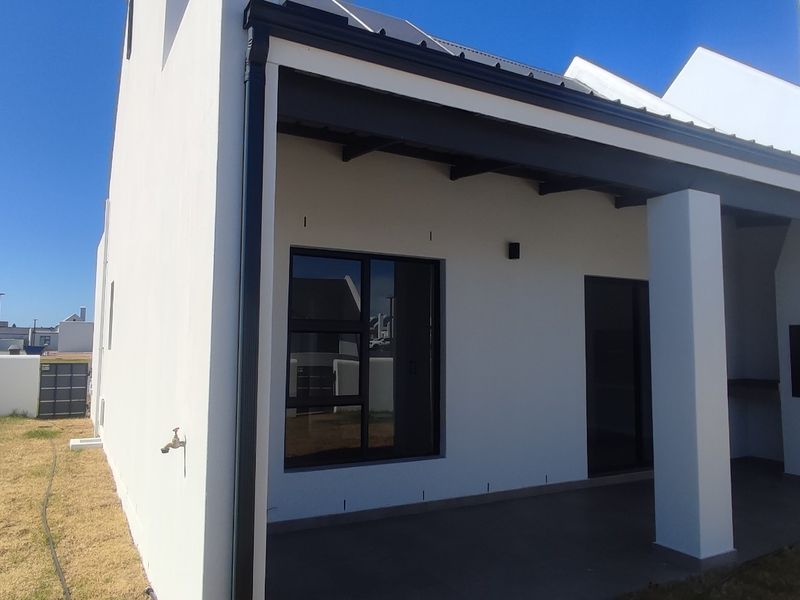 A modern covered patio featuring a built-in braai, tiled flooring, and exposed rafters, overlooking a private garden area.