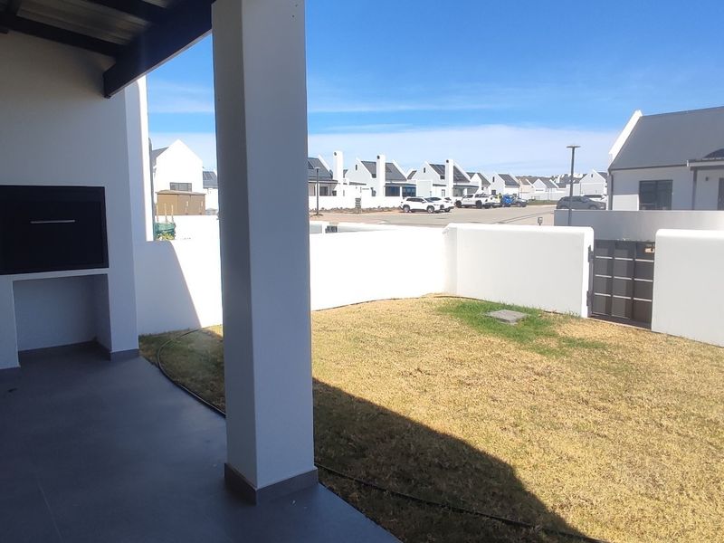 A covered patio area featuring a built-in braai, tiled flooring, and direct access to a private garden space with boundary walls.