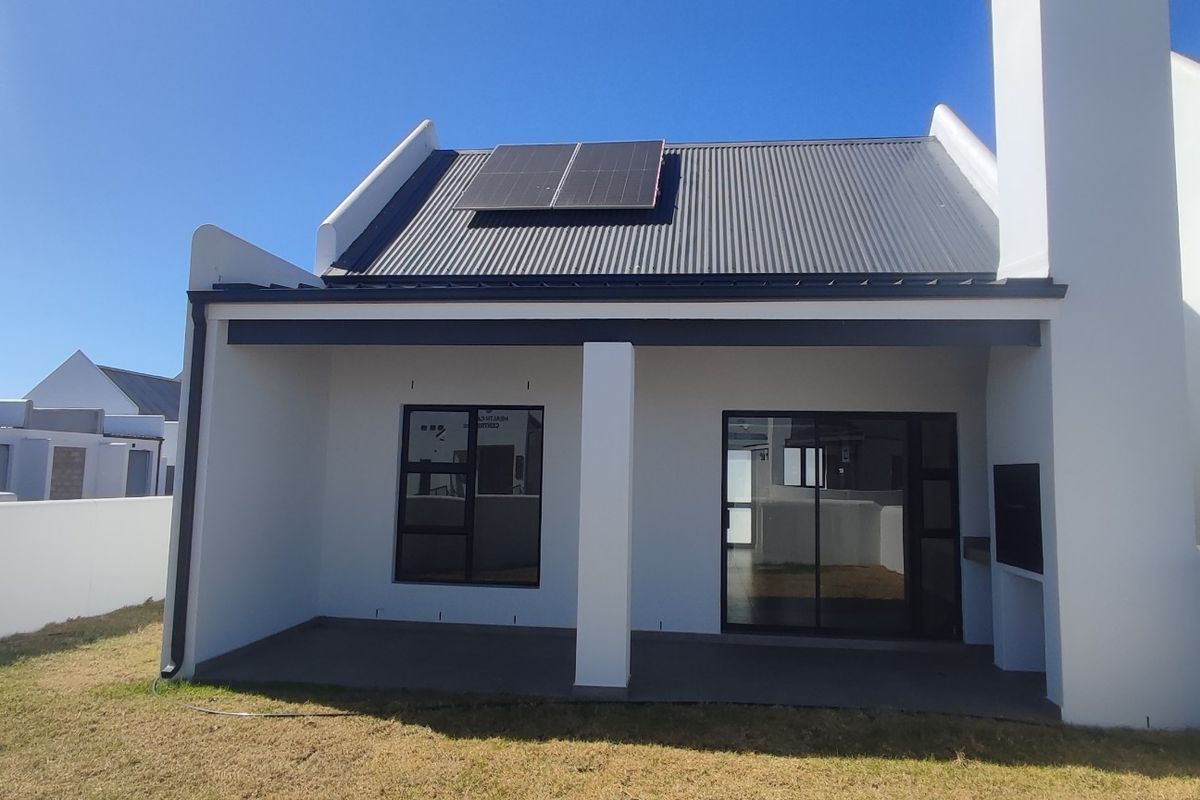 Rear view of a modern home featuring a covered patio with a built-in braai, sliding glass doors, and solar panels on a corrugated roof.