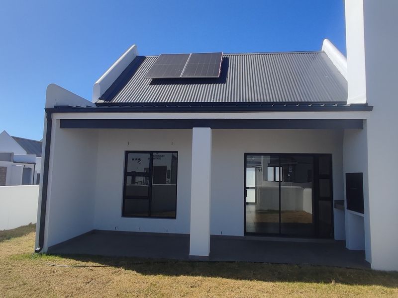 Rear view of a modern home featuring a covered patio with a built-in braai, sliding glass doors, and solar panels on a corrugated roof.