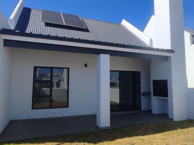 A covered patio area featuring a built-in braai, concrete flooring, and sliding door access, set against a modern white exterior with solar panels.
