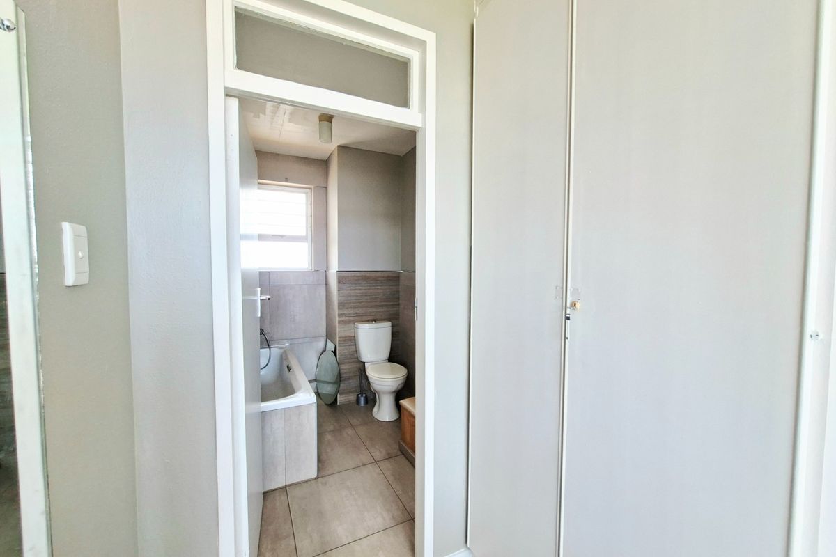 A view into a bathroom featuring a bathtub, toilet, and tiled finishes, adjacent to a hallway with built-in storage cupboards.