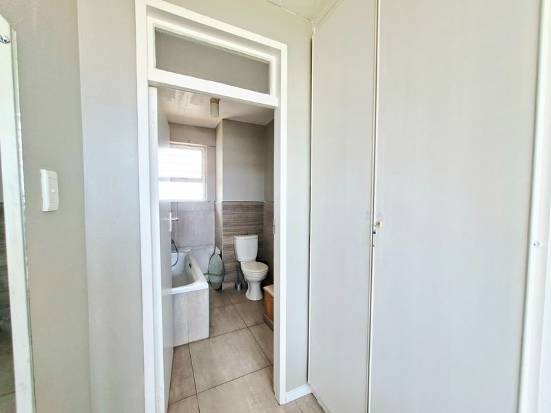 A view into a bathroom featuring a bathtub, toilet, and tiled finishes, adjacent to a hallway with built-in storage cupboards.