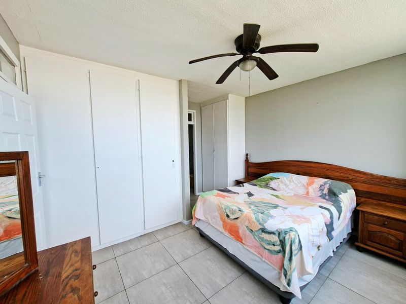 A bedroom featuring tiled flooring, a ceiling fan, and extensive built-in cupboard storage.