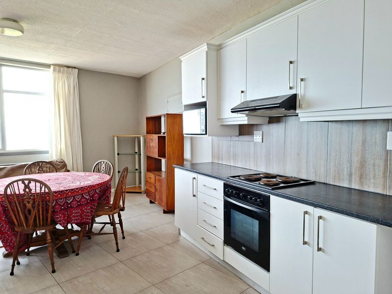 Open-plan kitchen and dining area featuring white cabinetry, built-in oven, electric hob, extractor fan, and neutral tiled flooring.