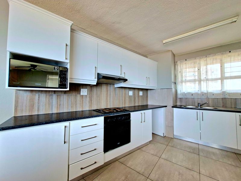A clean and functional kitchen featuring white cabinetry, dark laminate countertops, built-in oven and hob, and tiled flooring.