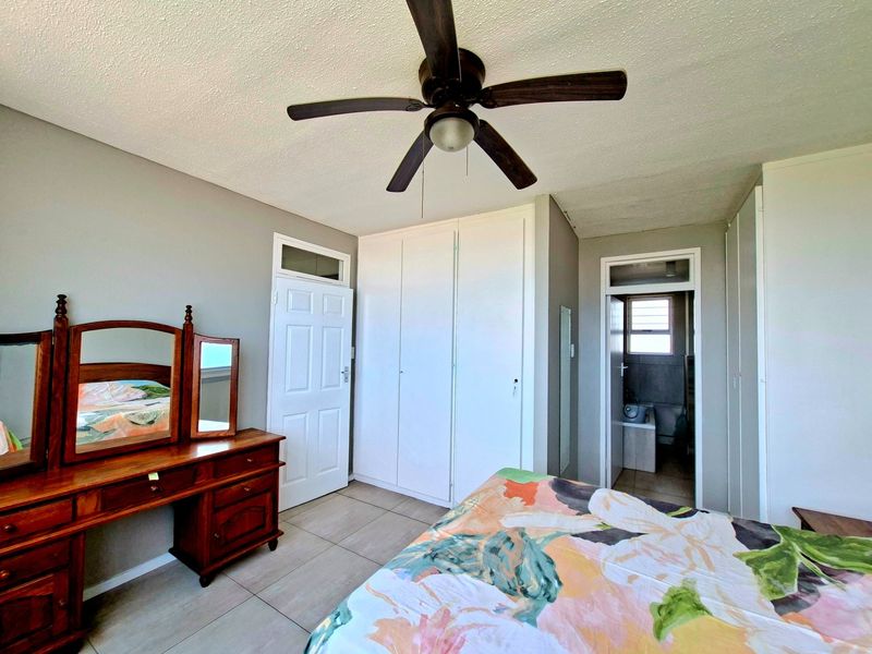 A bedroom featuring tiled flooring, built-in cupboards, a ceiling fan, and direct access to an en-suite bathroom.