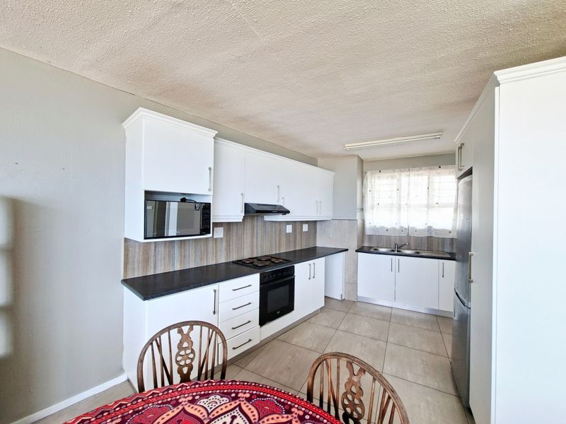 A functional kitchen featuring white cabinetry, dark laminate countertops, built-in oven with hob, extractor fan, and tiled flooring.