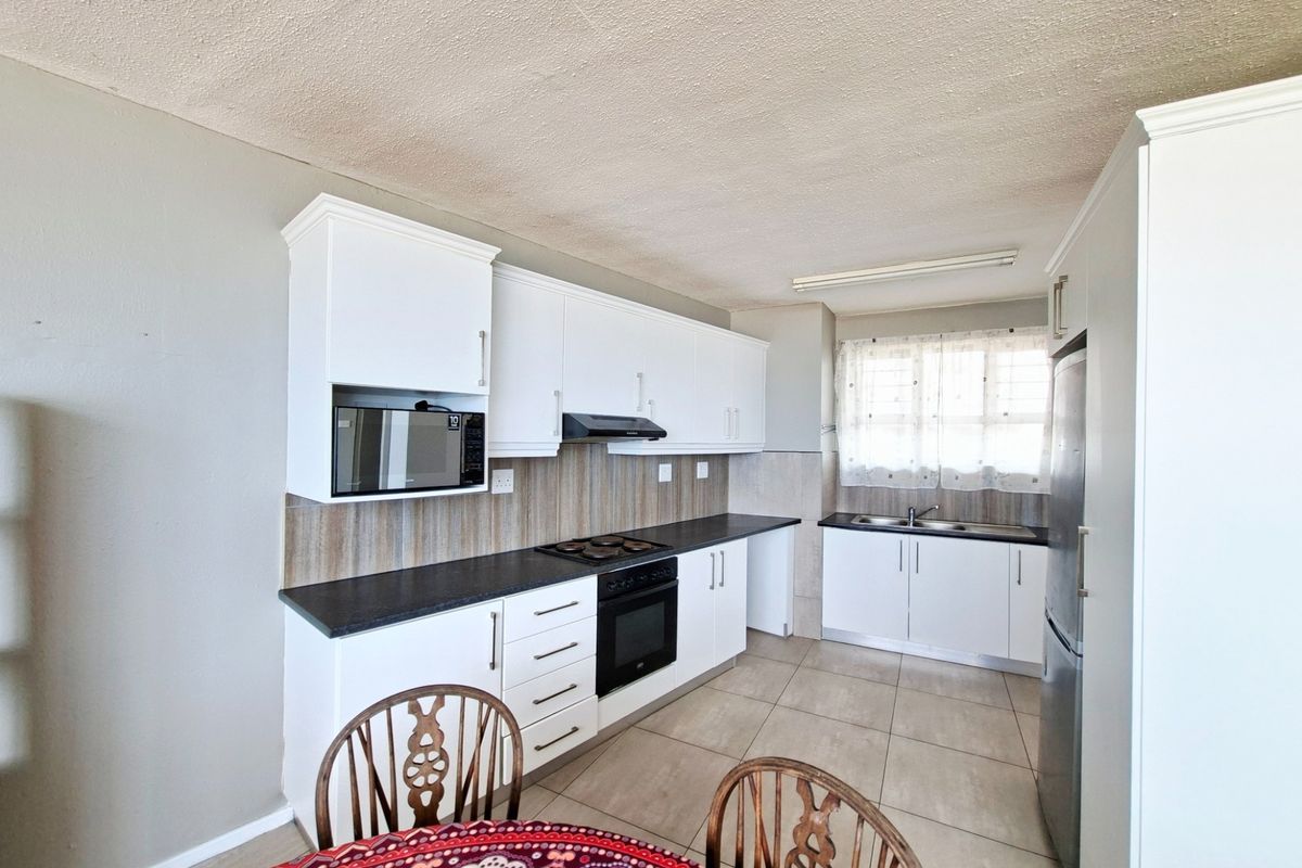 A functional kitchen featuring white cabinetry, dark laminate countertops, built-in oven with hob, extractor fan, and tiled flooring.