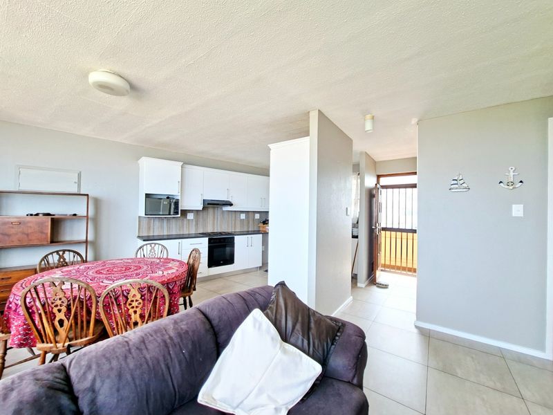 Open-plan living and kitchen area featuring tiled floors, white cabinetry, and direct access to an external entrance with a security gate.