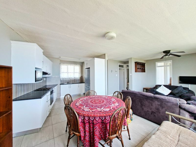 Open-plan living and kitchen area featuring white cabinetry, dark countertops, tiled flooring, and a ceiling fan, creating a functional and connected living space.