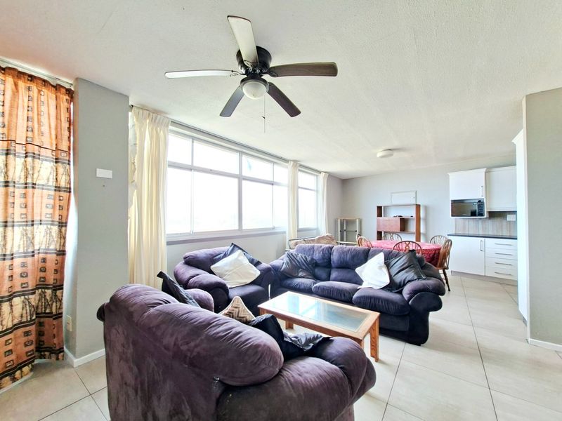 Open-plan living and kitchen area featuring tiled floors, a ceiling fan, and large windows providing ample natural light.