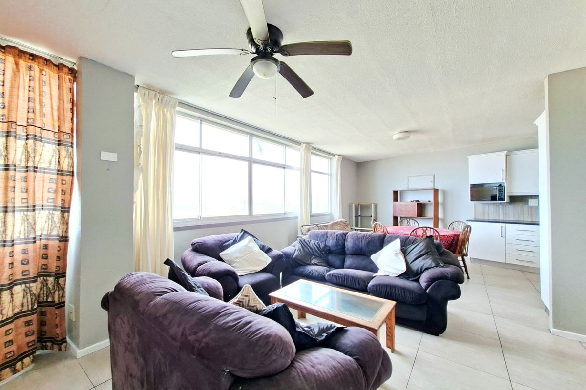 Open-plan living and kitchen area featuring tiled floors, a ceiling fan, and large windows providing ample natural light.