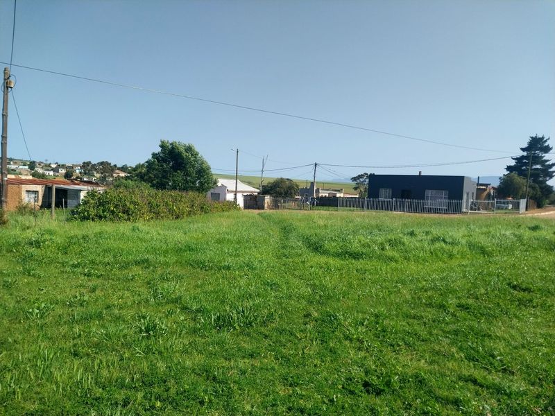A view of a vacant residential plot featuring grassy terrain, utility poles, and surrounding neighborhood infrastructure.