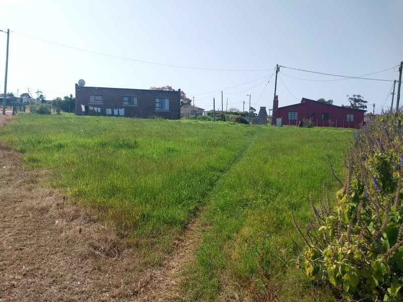 A view of a vacant residential plot featuring a grassy lawn, utility poles, and overhead power lines with neighboring houses in the background.