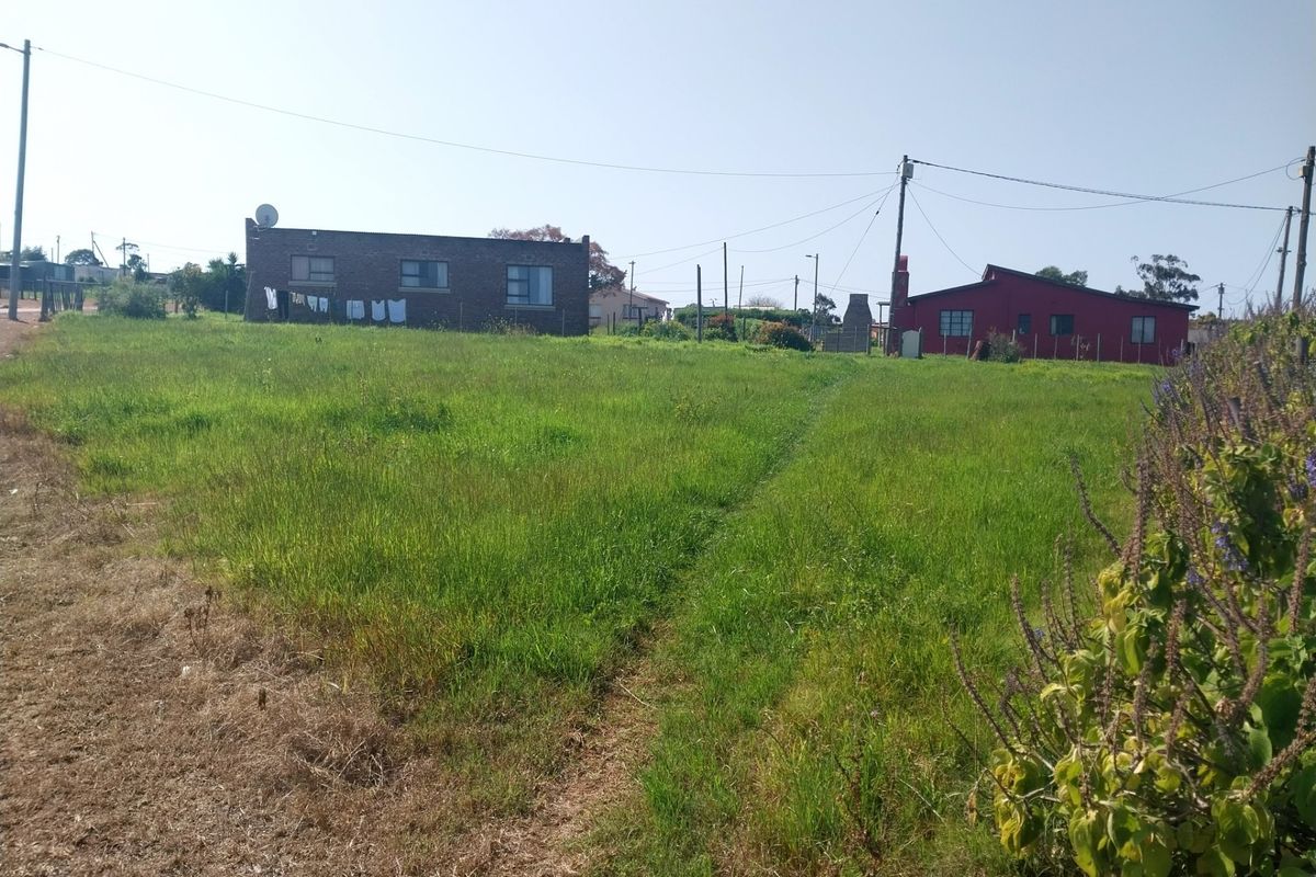 A view of a vacant residential plot featuring a grassy lawn, utility poles, and overhead power lines with neighboring houses in the background.