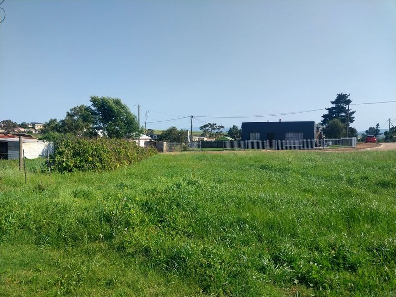 A view of a vacant residential plot featuring open grassland, perimeter fencing, and surrounding neighborhood infrastructure.