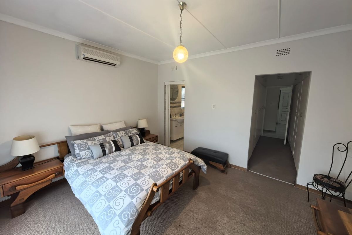 Spacious bedroom featuring carpeted flooring, an air conditioning unit, and direct access to an en-suite bathroom.