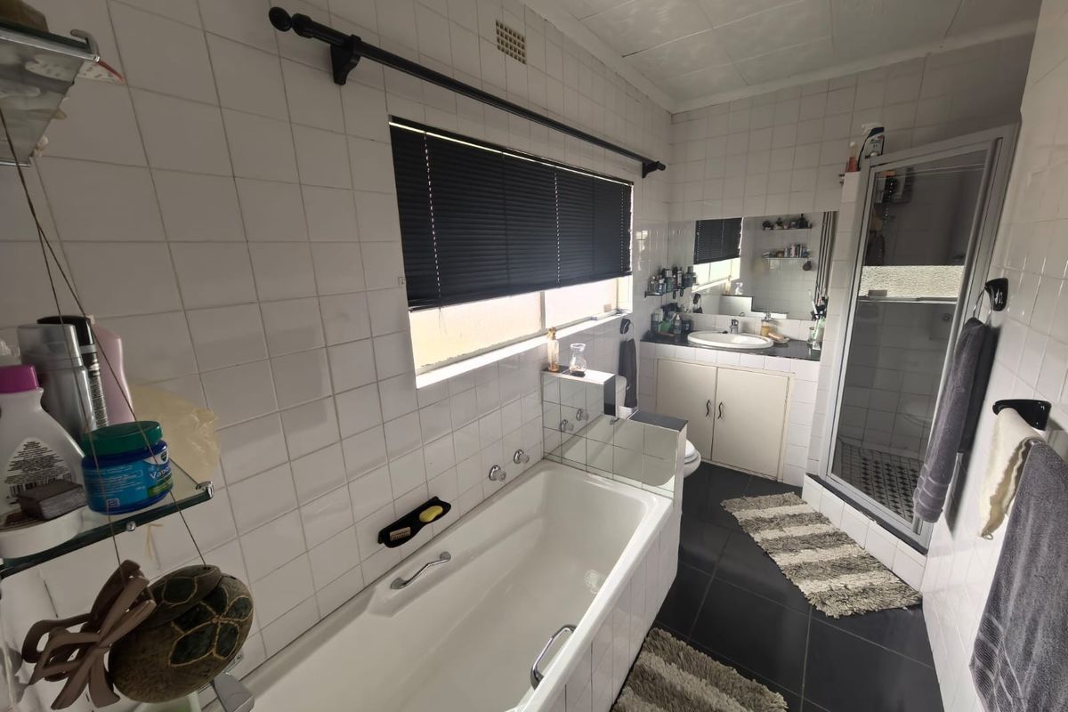 A functional bathroom featuring a built-in bathtub, separate shower enclosure, and a vanity cabinet with integrated mirror, finished with classic wall and floor tiling.