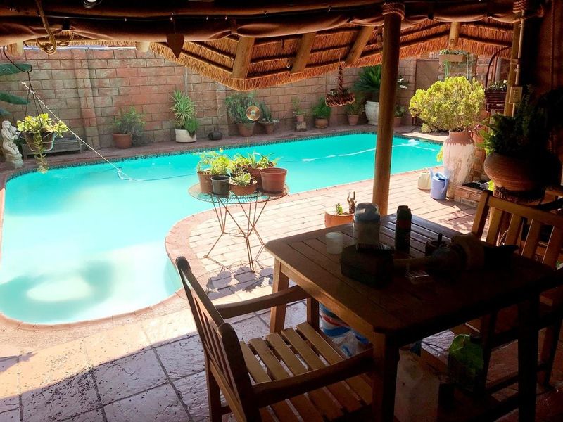 Outdoor entertainment area featuring a swimming pool, paved patio, and a covered thatched roof structure.