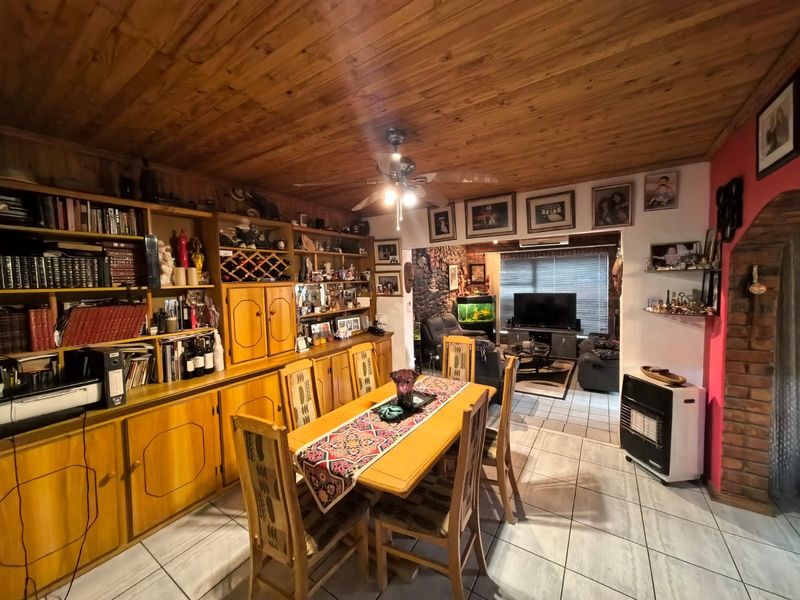 Open-plan living and dining area featuring a timber ceiling, built-in wooden cabinetry, tiled flooring, and a brick feature wall.