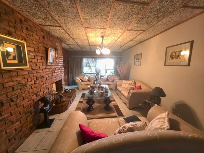 A living room featuring a prominent brick fireplace, tiled flooring, and a textured ceiling, offering a traditional layout with natural light.
