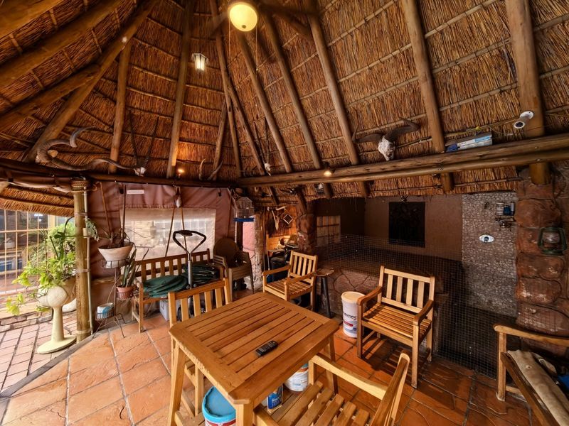 A rustic outdoor patio area featuring a traditional thatched roof, exposed timber rafters, and terracotta tiled flooring, providing a covered space for outdoor relaxation.
