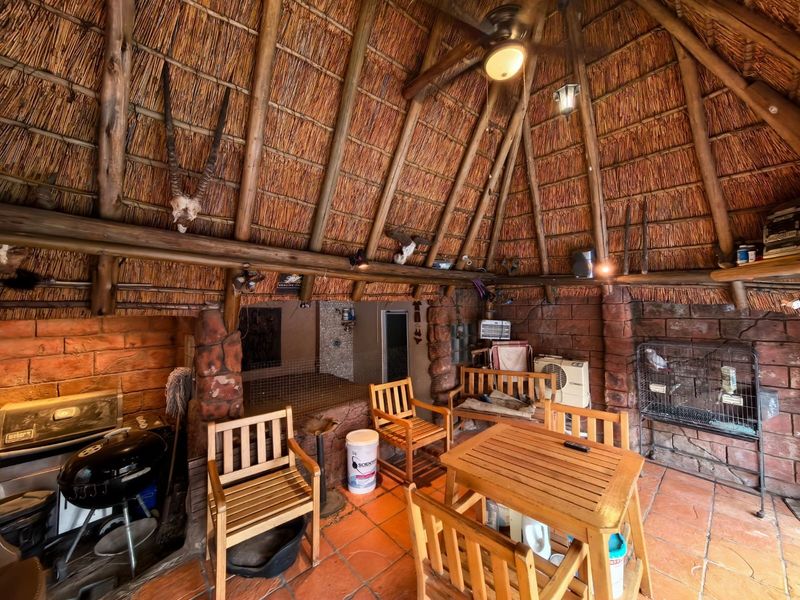 Covered outdoor patio area featuring a traditional thatched roof, exposed timber rafters, stone-clad pillars, and terracotta tiled flooring.
