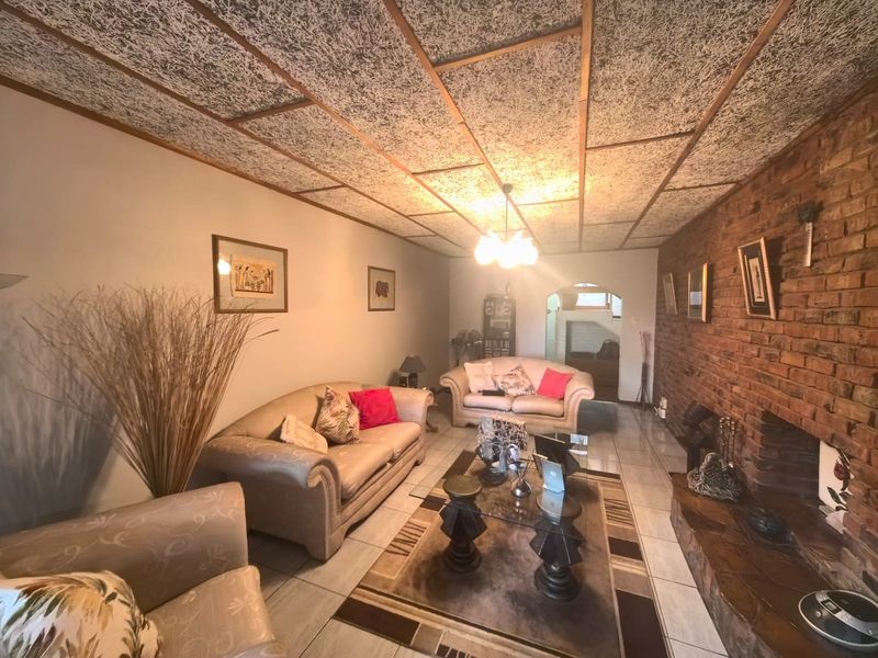 Spacious living room featuring an exposed brick wall, a built-in fireplace, and distinctive textured ceiling tiles with tiled flooring throughout.