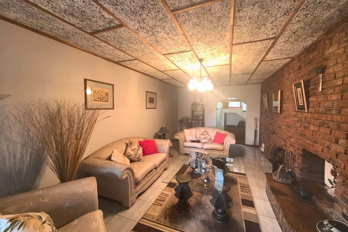 Spacious living room featuring an exposed brick wall, a built-in fireplace, and distinctive textured ceiling tiles with tiled flooring throughout.