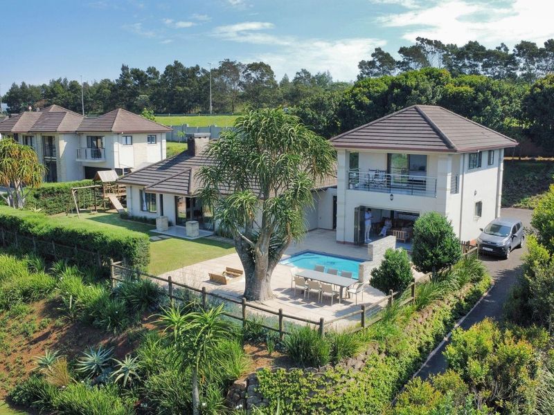 Aerial view of a residential property featuring a swimming pool, paved patio area, landscaped garden, and a multi-level house with a tiled roof.