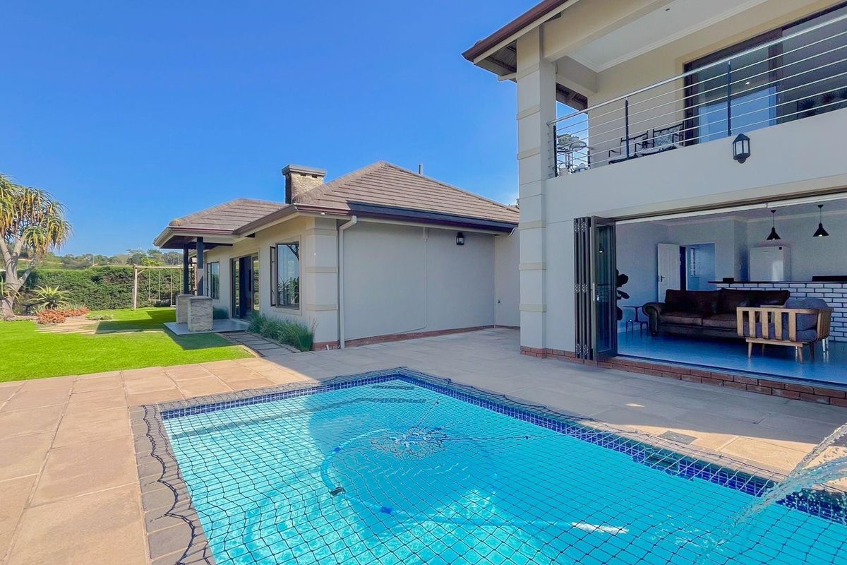 Spacious rear exterior featuring a swimming pool with safety net, tiled patio area, and a double-story structure with a balcony and folding glass doors.