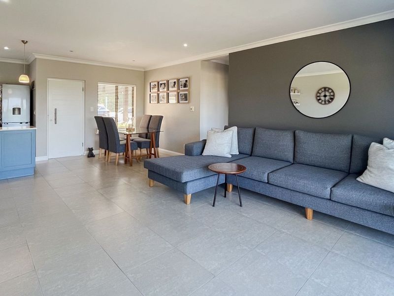 Spacious open-plan living area featuring a modern kitchen island, neutral tiled flooring, and a contemporary grey feature wall.